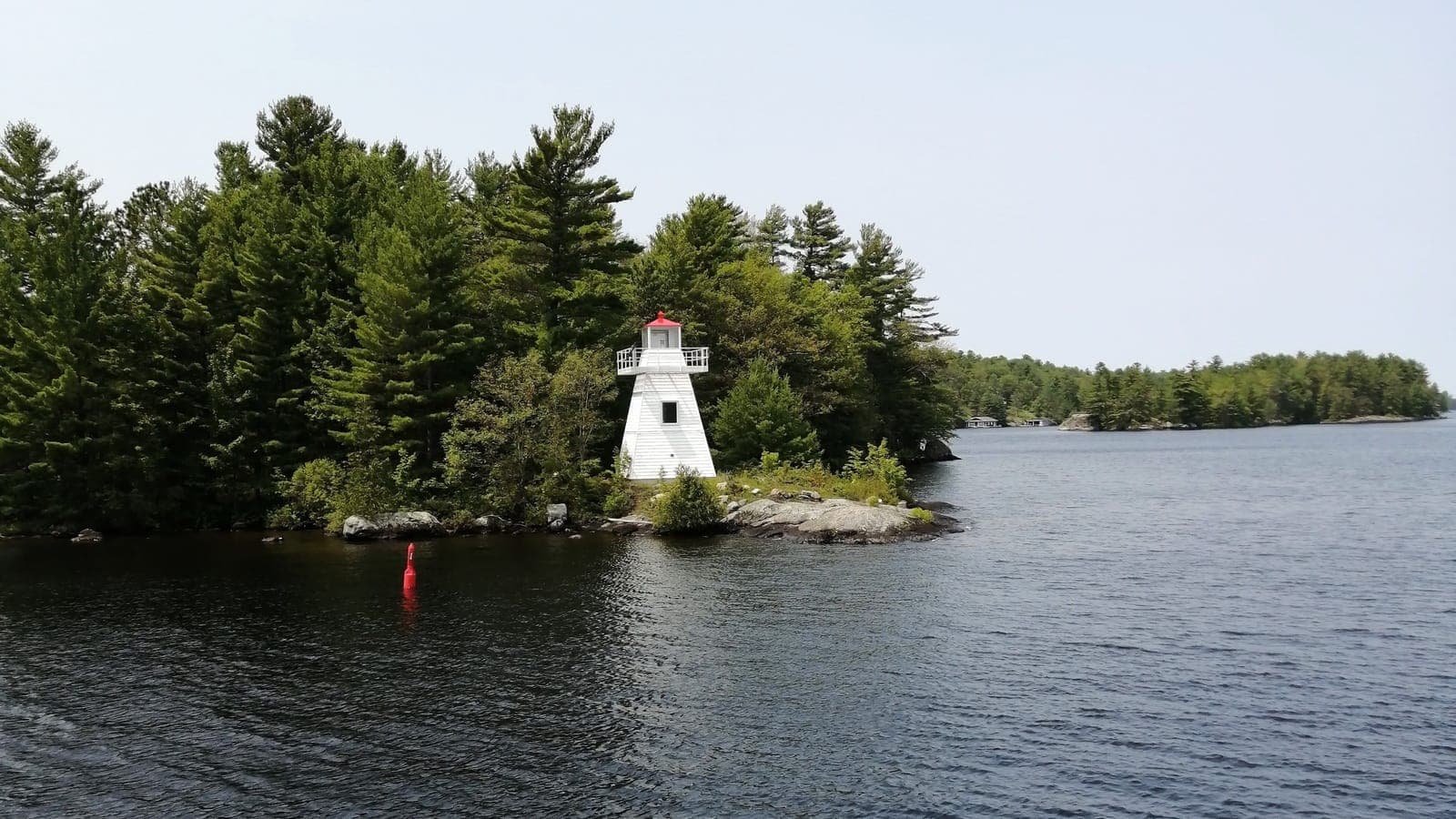 A small white lighthouse at the tip of a pine-covered island, with open water stretching away past it.